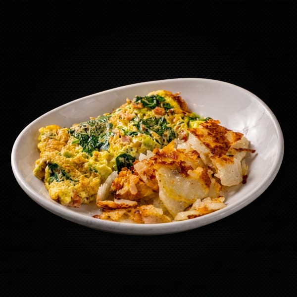 A white oval plate holds a spinach and cheese omelet with a side of crispy hash browns.