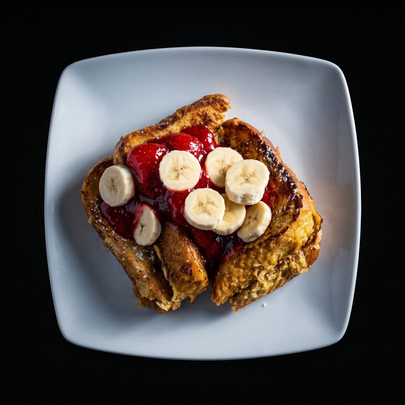 Golden French toast topped with strawberry compote and sliced bananas on a white plate.